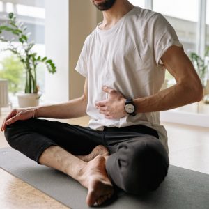 man in white shirt and black pants sitting on yoga mat