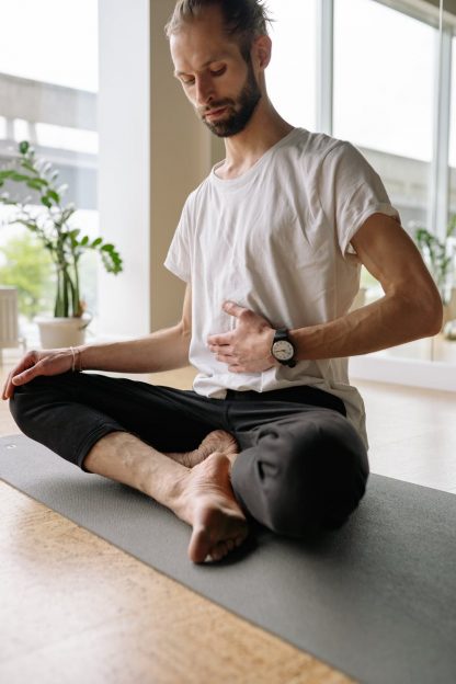 man in white shirt and black pants sitting on yoga mat